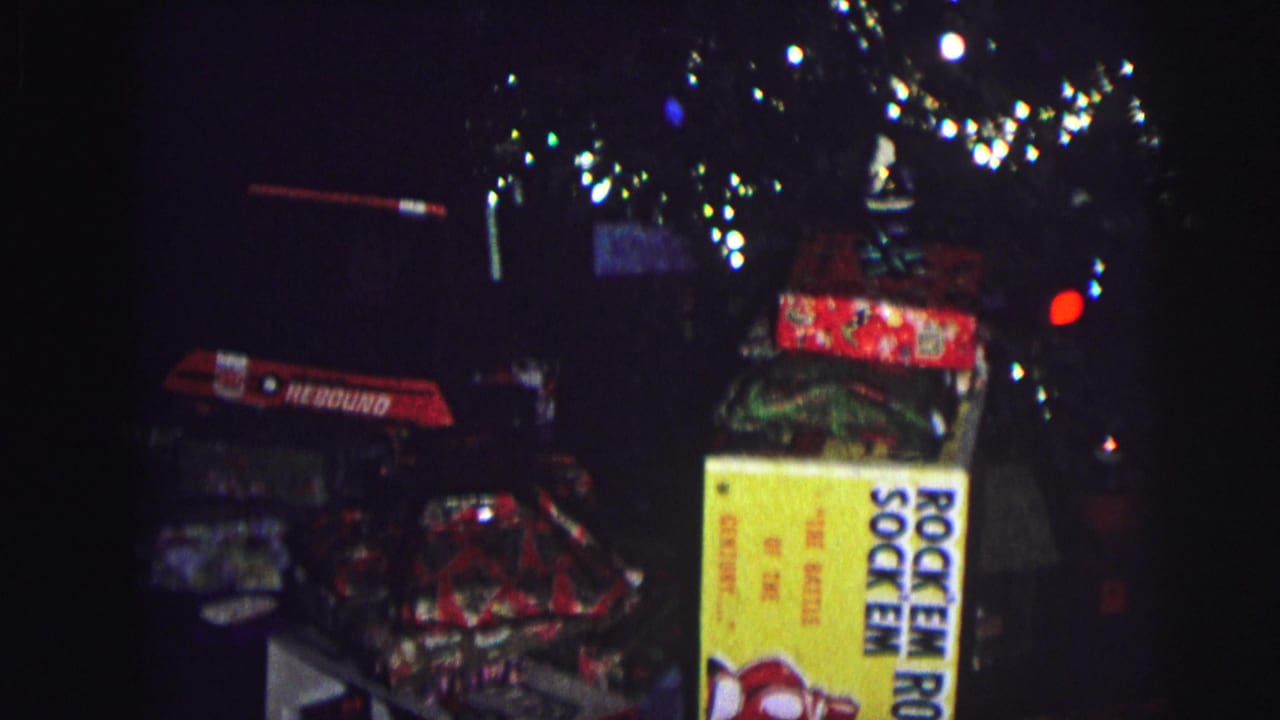 Christmas tree with colored lights and wrapped presents; a yellow Rock 'Em Sock 'Em Robots box and a second branded game box are visible in a dark interior.
