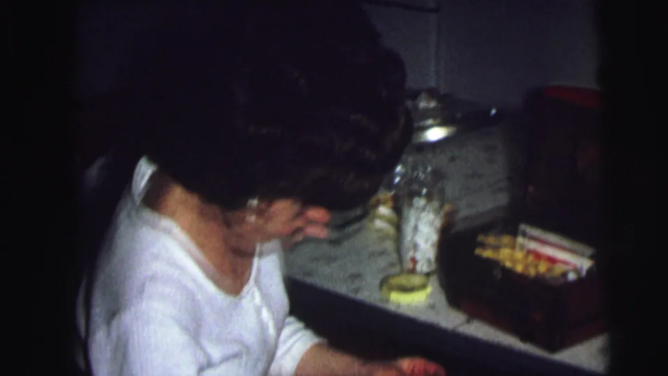Woman in white top at kitchen counter with jars and snack items, 8mm home movie, Lynbrook NY, 1976.