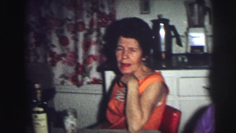 Woman in orange sleeveless dress at kitchen counter with floral curtains and chrome percolator, 8mm home movie, Lynbrook NY, 1976.