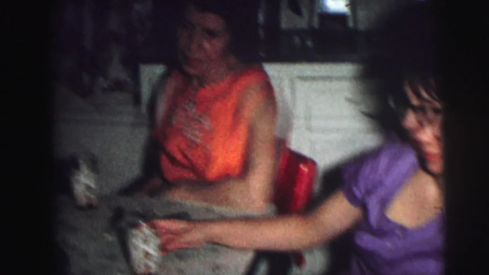 Two women at a kitchen counter, one in an orange top and one in purple, 8mm home movie, Lynbrook NY, 1976.