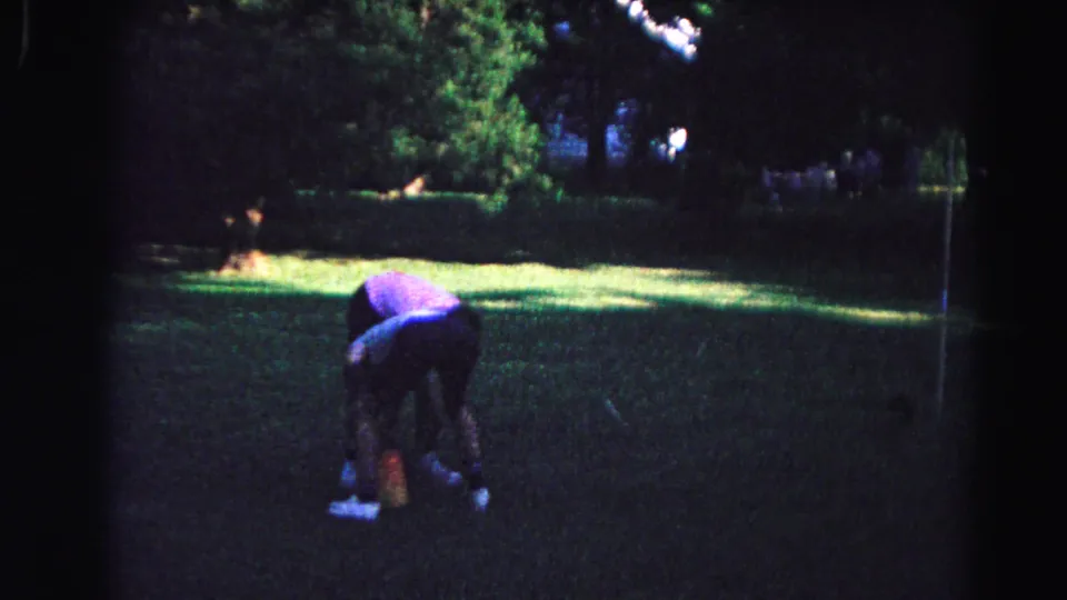 At the end of the clip, a person bends over on the backyard lawn, with deep shade, green grass, and trees visible in the 1963 home-movie frame.
