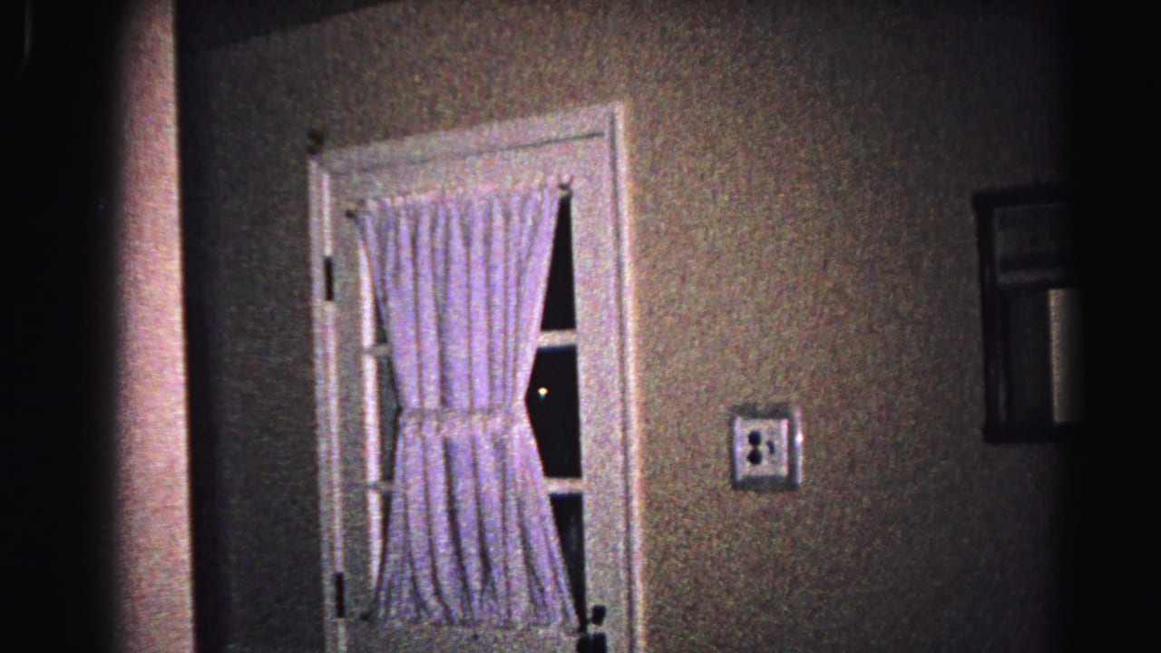 Dimly lit white-framed door with gingham curtains set in a textured wall, viewed from inside the home.