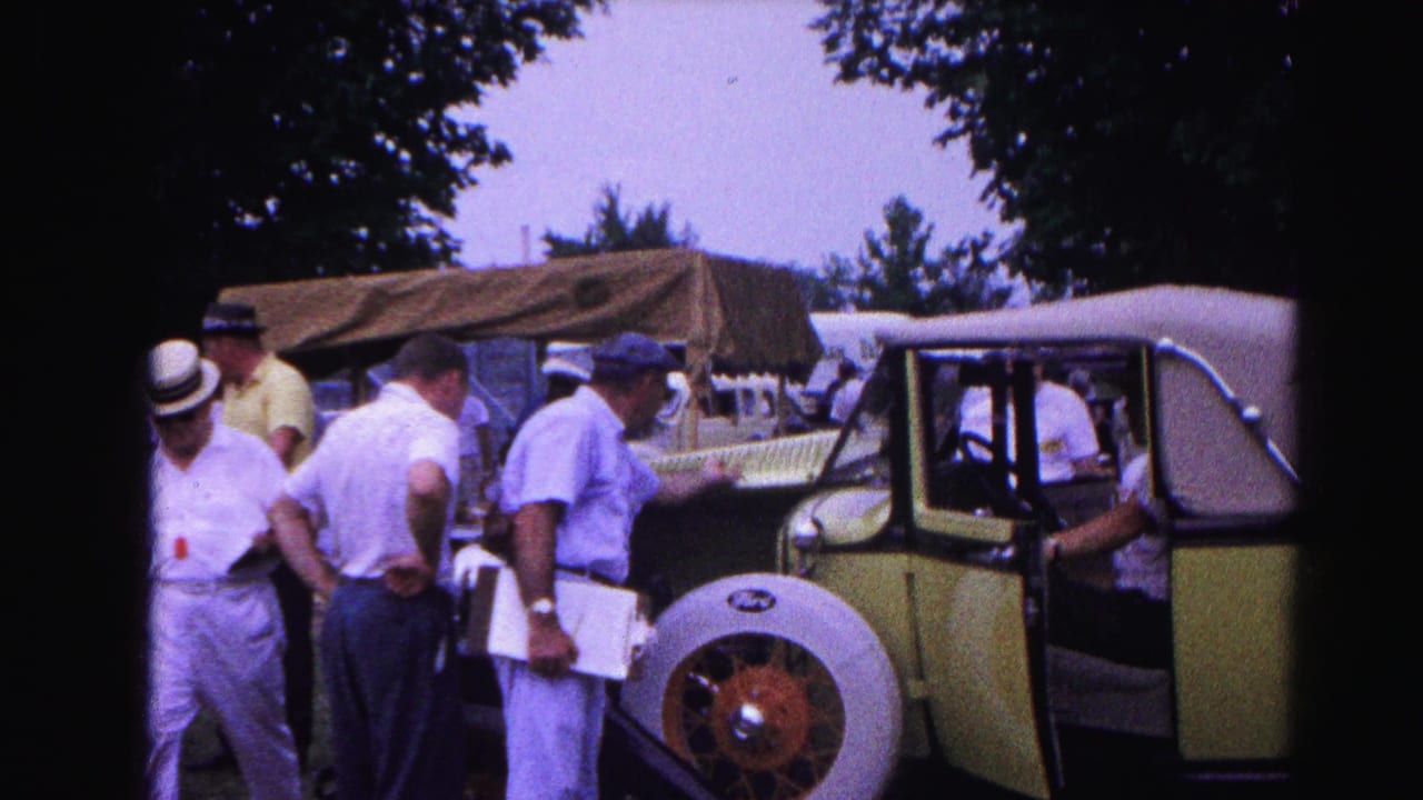 Group of men in early-1960s summer attire, including straw hats, gathered around a yellow-green open-top vintage automobile at an outdoor car show, Hagerstown, Maryland, circa 1963.