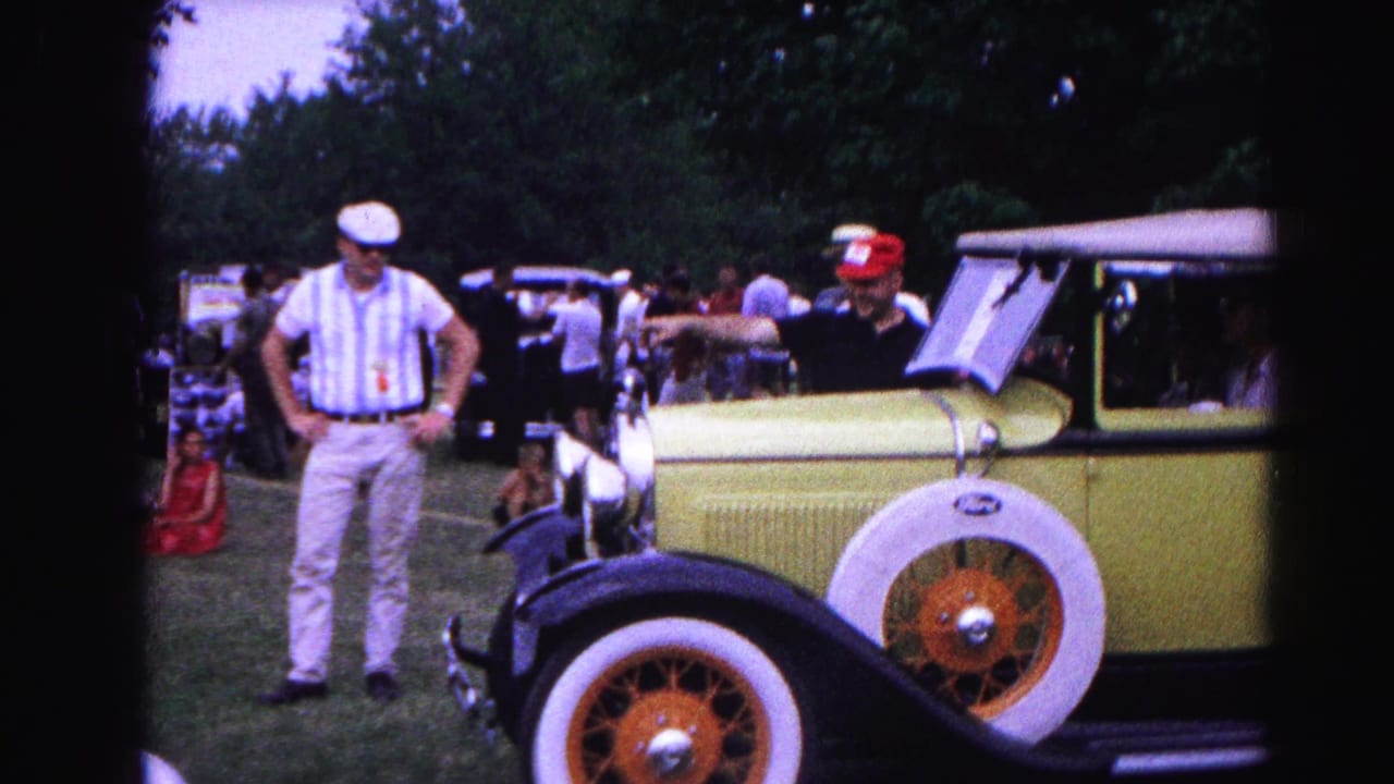 A yellow vintage Ford convertible with whitewall tires sits on grass at a 1963 Hagerstown, Maryland car show as spectators stand around it.