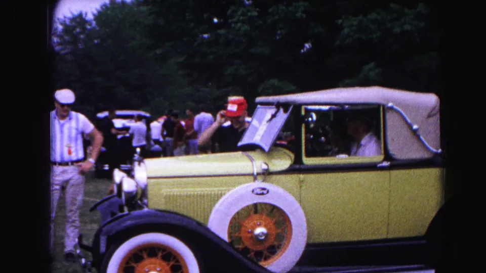 Side view of the yellow Ford convertible at the Maryland car show, with a display placard on the windshield and spectators gathered around the driver's side.