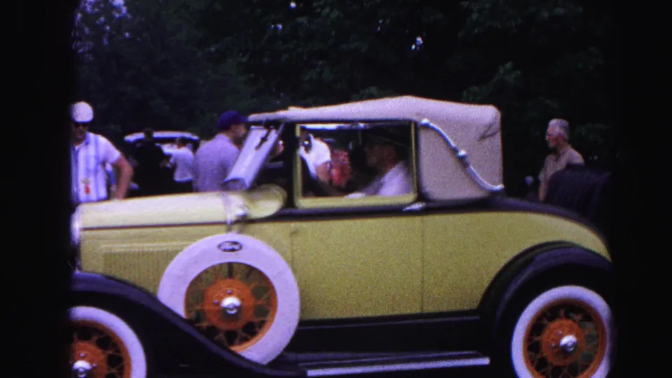 The yellow Ford convertible fills the frame at the 1963 Hagerstown car show, with people visible inside and around the vehicle against a tree-lined background.