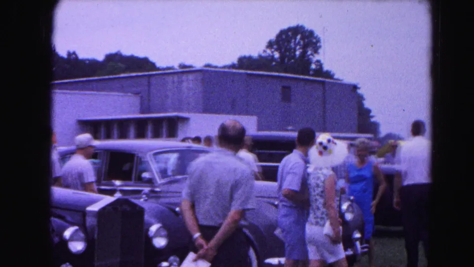 Adults in early-1960s summer attire gathered around large dark classic automobiles at what appears to be an outdoor car show, consistent with 1963 Hagerstown, Maryland.