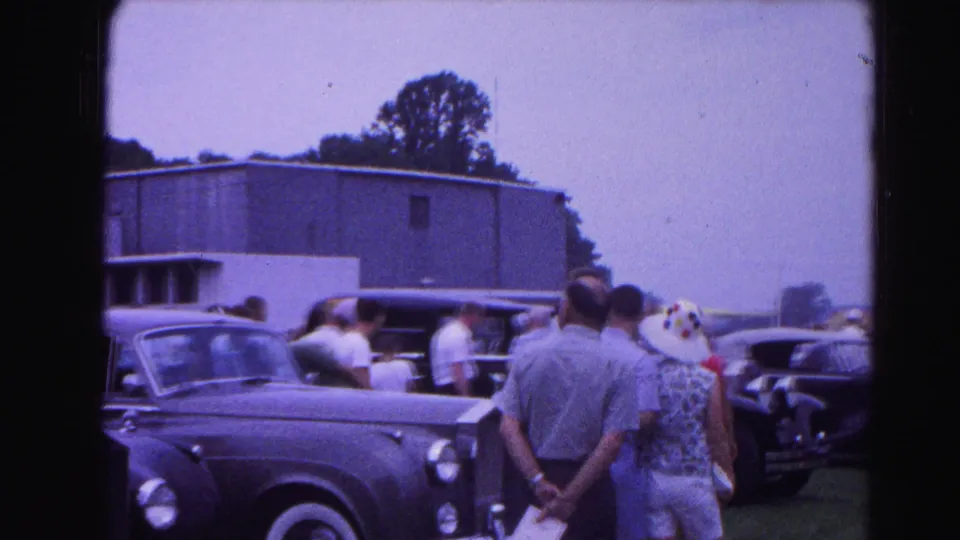 Outdoor car show attendees, mostly seen from behind, examine dark classic automobiles; 8mm footage consistent with early 1960s Hagerstown, Maryland.
