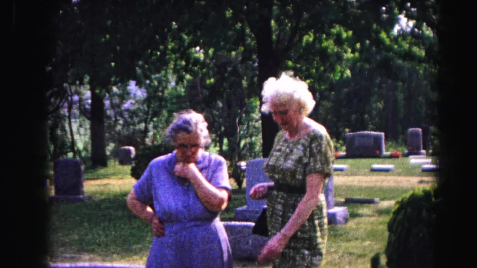 Two elderly white-haired women standing among granite headstones in a tree-lined cemetery, likely Hagerstown, Maryland, circa 1963, 8mm home movie.