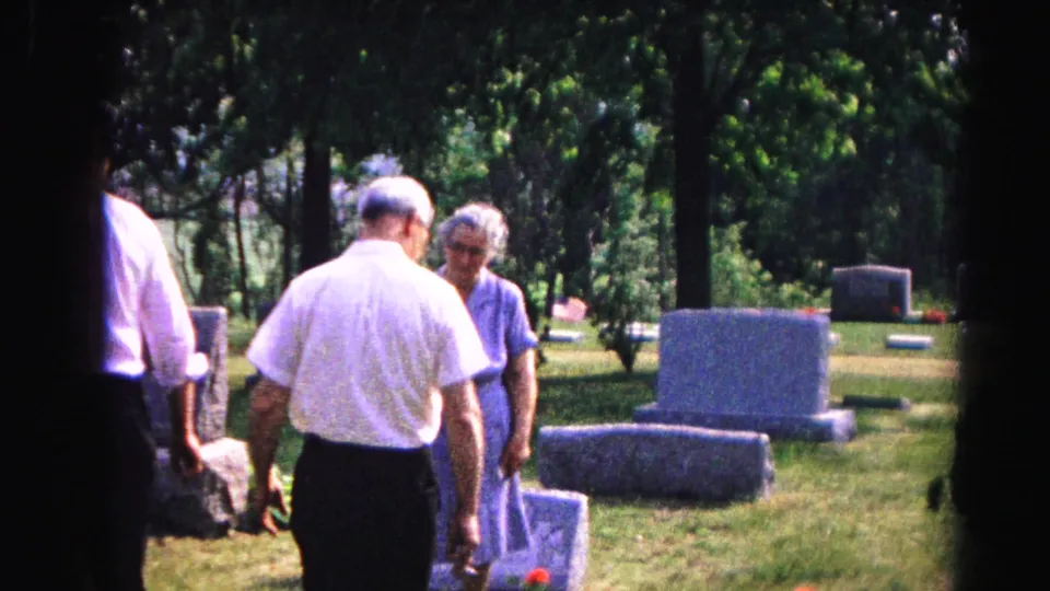 Four people, two men in white shirts and two elderly women, walking together in a cemetery, circa 1963, filmed on 8mm home movie stock.