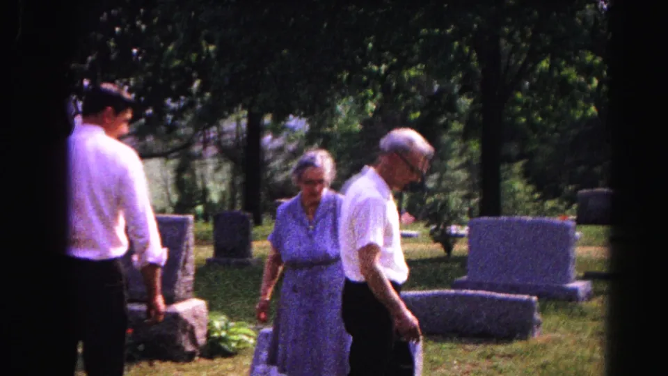 Four adults walking slowly through a tree-lined cemetery together, consistent with Hagerstown, Maryland circa 1963, filmed on 8mm home movie stock.