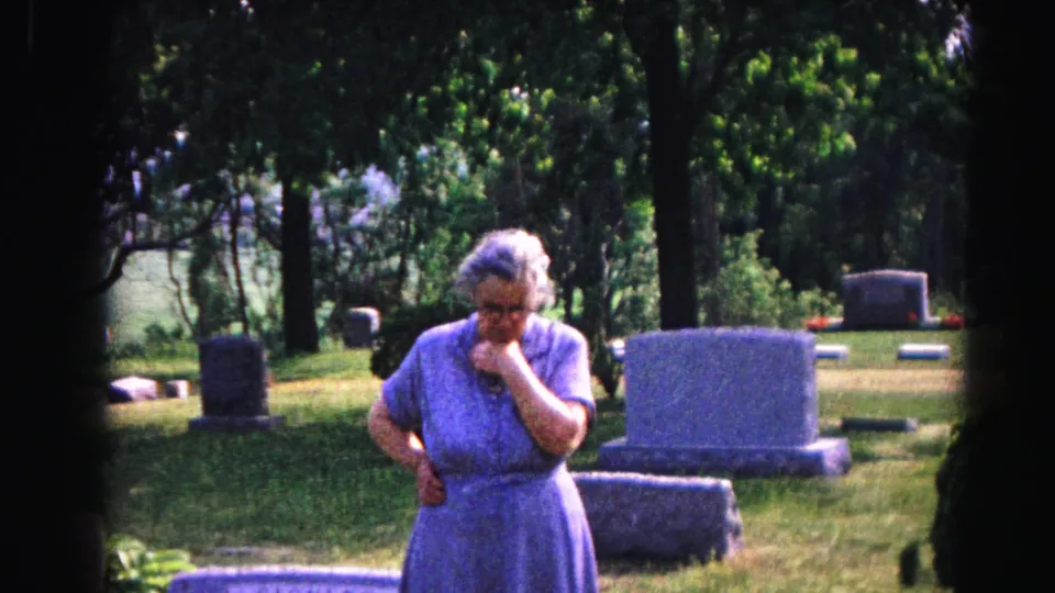 Elderly woman bowing head in grief at a sunlit cemetery, 8mm home movie circa 1963, Hagerstown, Maryland.