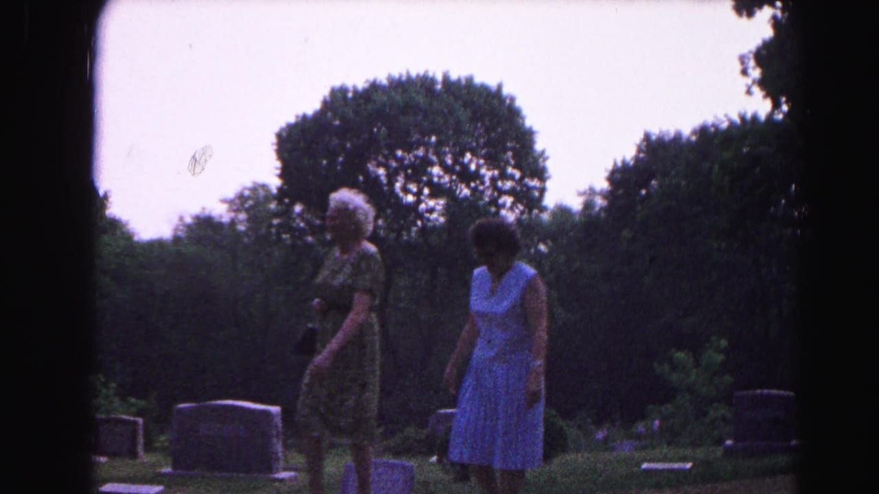Two women in 1960s summer dresses pause among gravestones in Hagerstown, Maryland, circa 1963, with dense summer trees framing the scene.