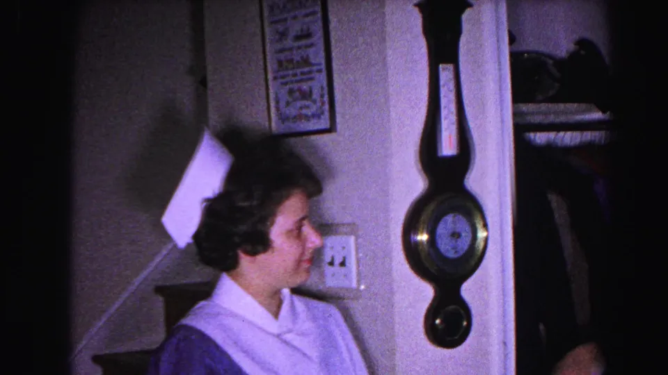 Young woman in white nurse's cap and dress uniform in a 1960s home hallway, Hagerstown, Maryland; a decorative wall barometer hangs beside her.