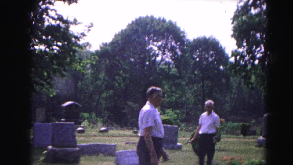 Two men walking among grave markers in a lush, tree-lined cemetery, possibly Hagerstown, Maryland area, c. 1963.