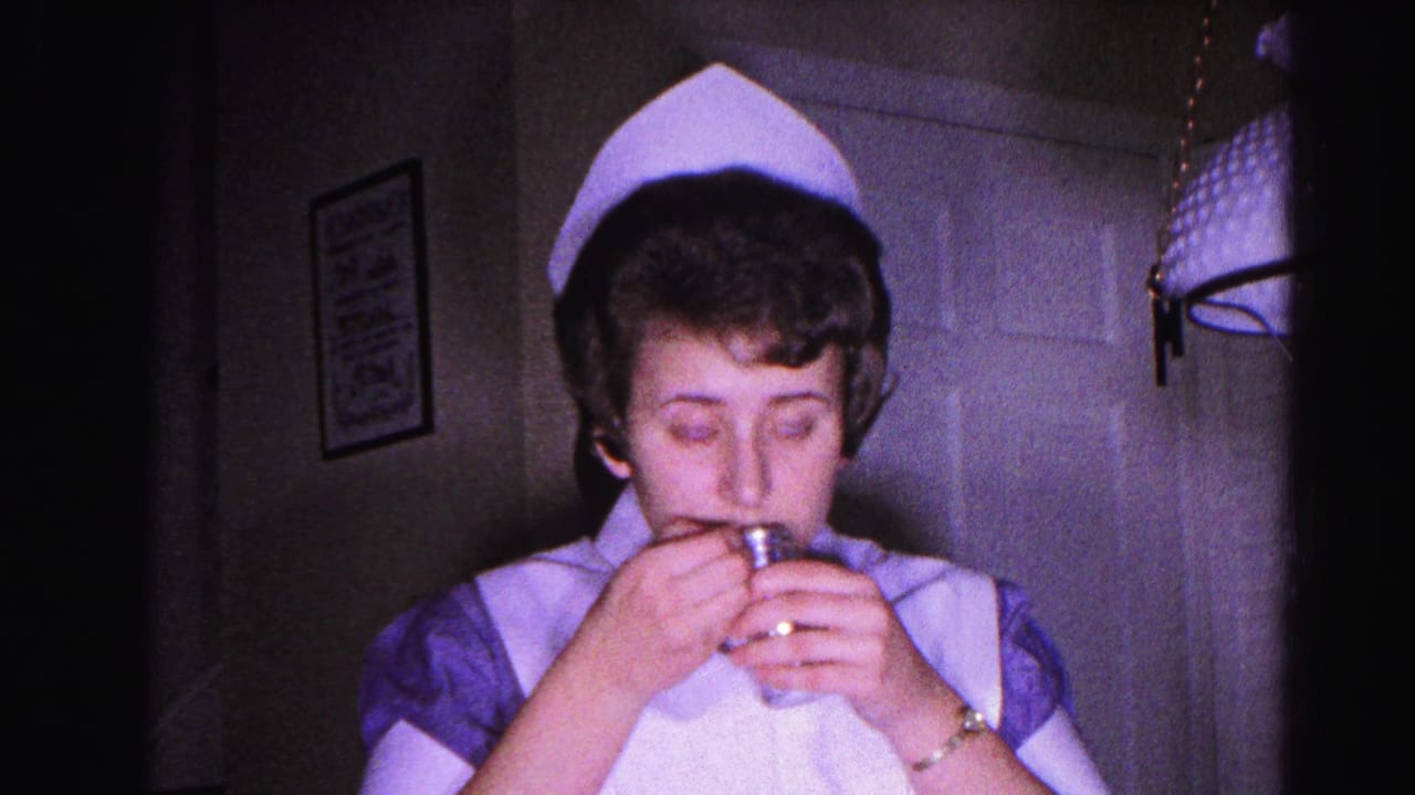 Woman in nurse uniform raises a small bottle toward her face in a dim room interior.