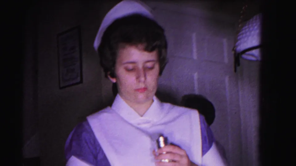 Close-up of 1960s-uniformed nurse with starched white cap, holding a small elongated item; face clearly visible; 8mm home movie, Hagerstown, Maryland, 1963.