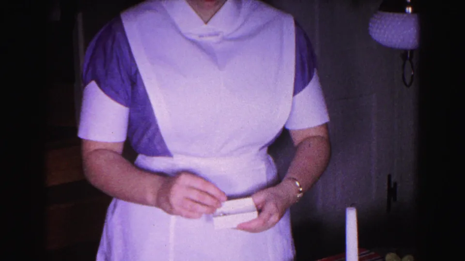 1963 8mm home movie: woman in blue dress and apron holds flat gift item in a holiday domestic setting, Hagerstown, Maryland.