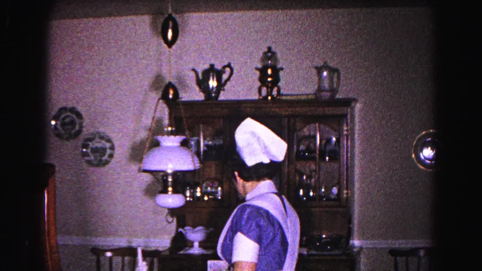 Profile view of young woman in 1960s nurse's uniform with cap near a hanging lavender parlor lamp in a domestic dining room, Hagerstown, Maryland, circa 1963.