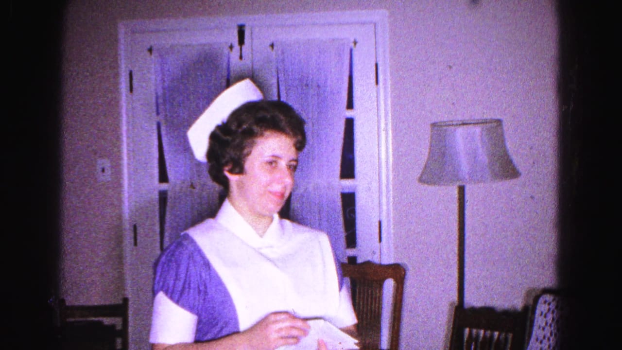 Woman in nurse uniform looks up and to the side with a smile, holding a paper; window, floor lamp, and wooden chair visible behind her.