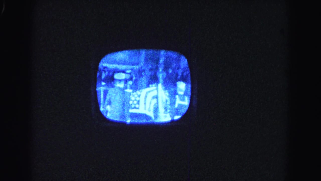 Vintage rounded-corner CRT television glowing blue-white in a darkened room, showing a grainy black-and-white broadcast.