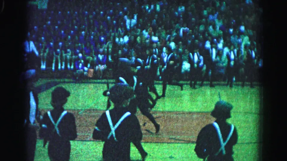 1963 Hagerstown, Maryland: three to four uniformed marchers with white X-cross-straps moving across the field; densely packed spectator crowd fills the background.