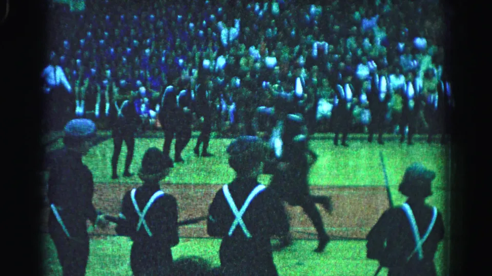 1963 Hagerstown, Maryland: close-medium shot of uniformed marchers with white X-cross-straps mid-stride; spectators visible across the full background.