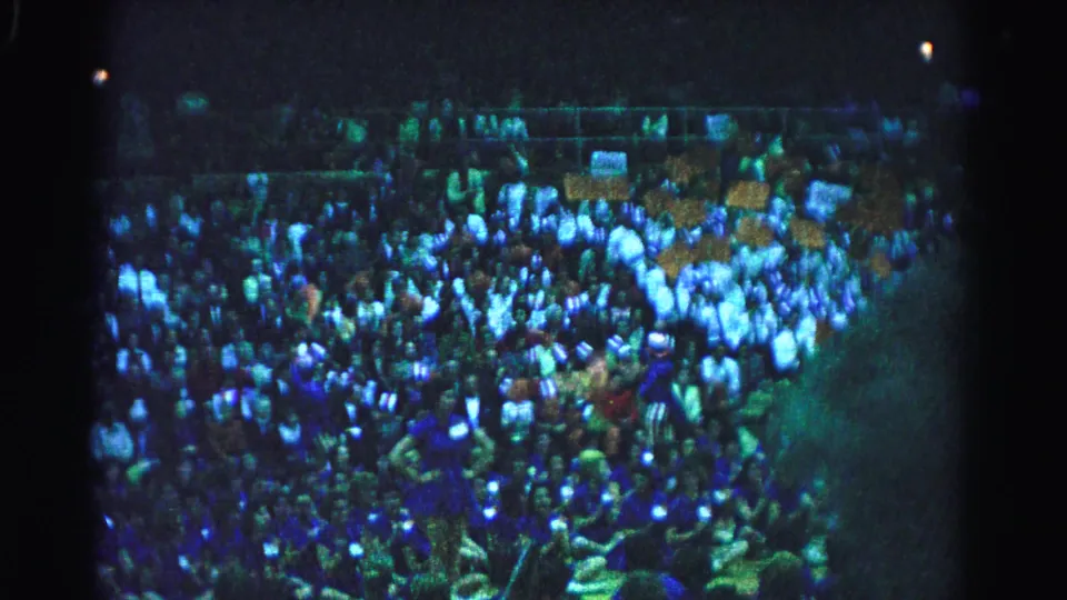 Crowd in stadium stands under artificial lighting, Hagerstown, Maryland, circa 1963; signs visible throughout, blue-green 8mm color shift present.
