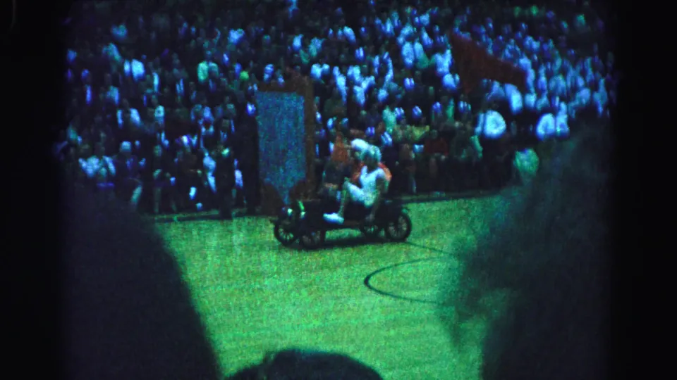 Two costumed performers on a small custom vehicle traverse a green basketball court floor at an apparent 1963 arena event in Hagerstown, Maryland, captured on 8mm film.