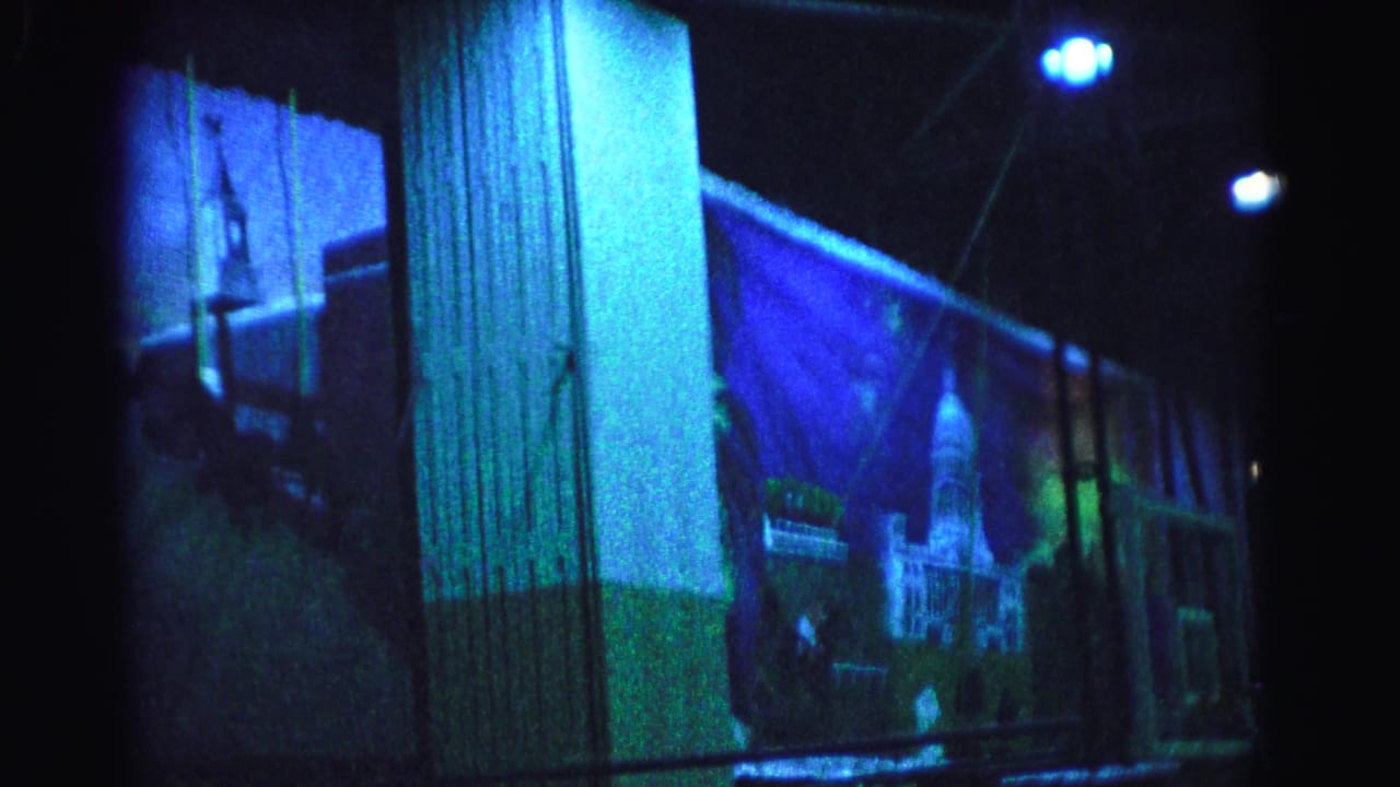 Dark gymnasium interior lit in blue-green with a large painted mural of a cityscape on the far wall and pendant ceiling lights visible above.