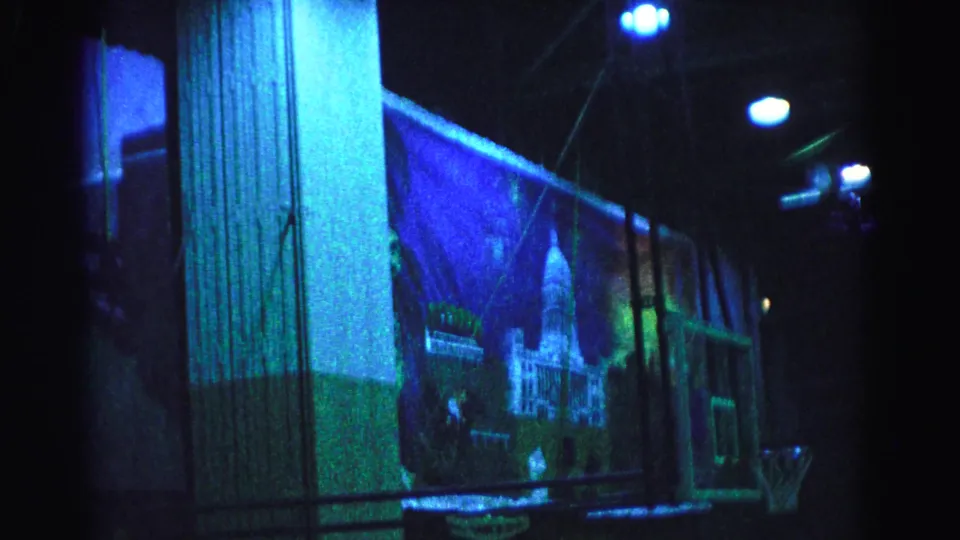 8mm footage circa 1963, Hagerstown Maryland — gymnasium interior with large decorative mural under blue stage lighting, basketball equipment and ceiling structure visible.