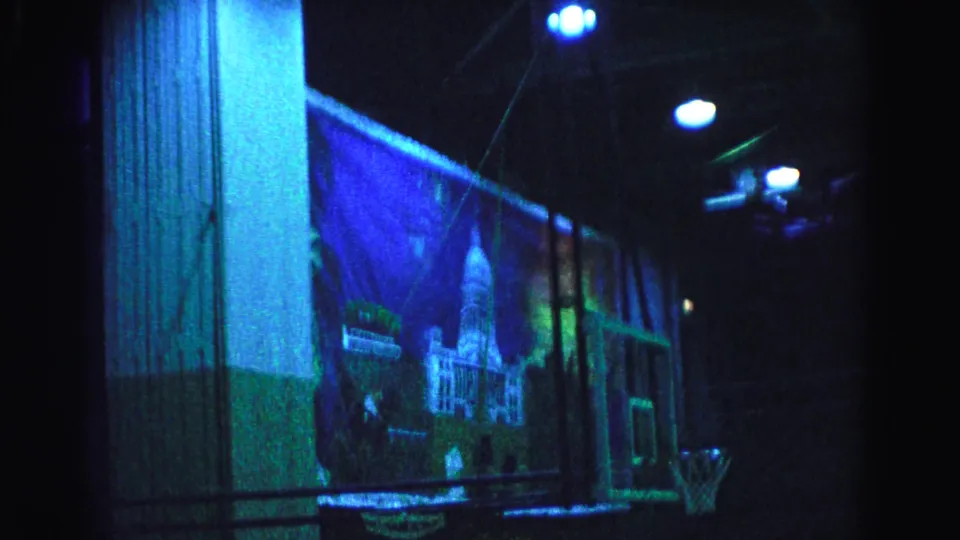 8mm home movie circa 1963, Hagerstown Maryland — gymnasium interior with large cityscape mural and pendant ceiling lights under low blue-green stage lighting.