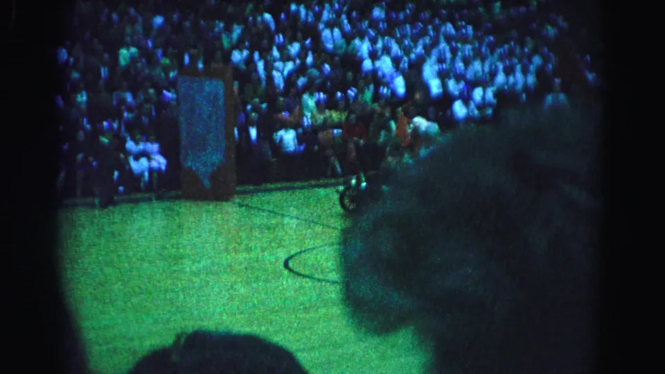 8mm home movie circa 1963, Hagerstown Maryland — overhead view of packed gymnasium crowd at a community event; person using wheelchair visible in foreground, decorated mural wall behind.