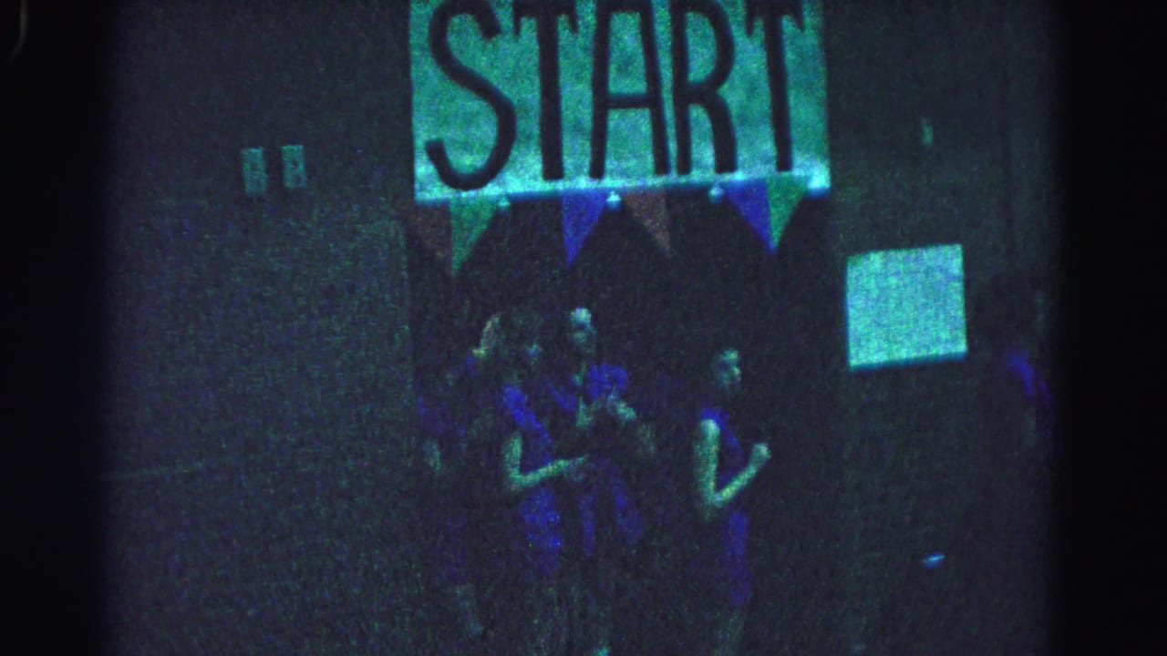 Two teenage girls in blue dresses stand beneath a START sign and triangular bunting, similar composition to the opening frame.