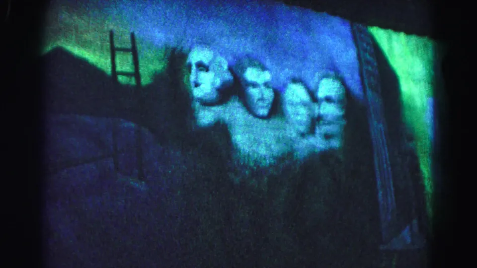 The Mount Rushmore projection continues in a dimly lit venue during a 1963 patriotic event in Hagerstown, Maryland; ladder and heavy film grain visible.