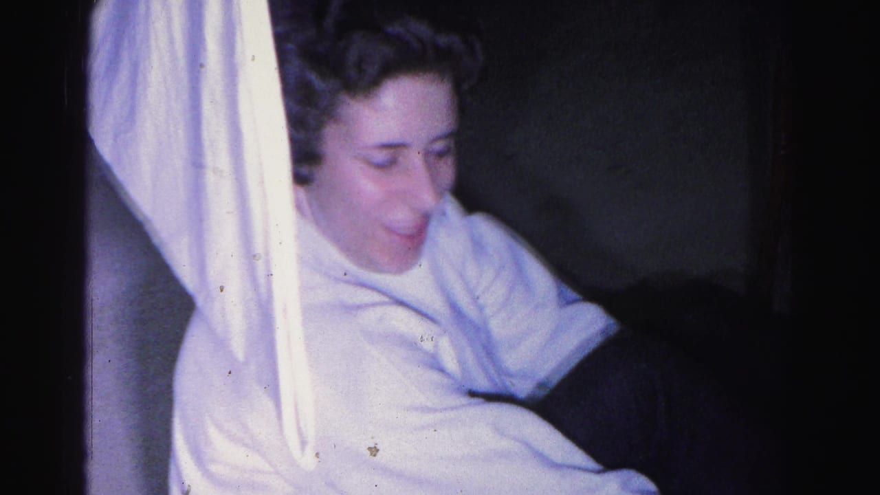 Young woman in white shirt sits near white fabric, looking downward, in a dim interior