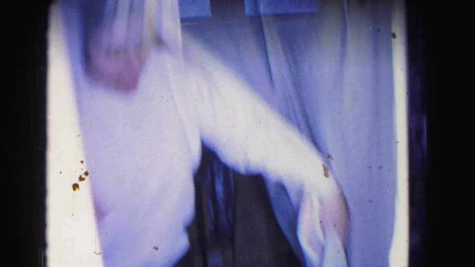 Motion-blurred figure in white garment near white fabric; 8mm emulsion spots and grain consistent with 1963 archival stock