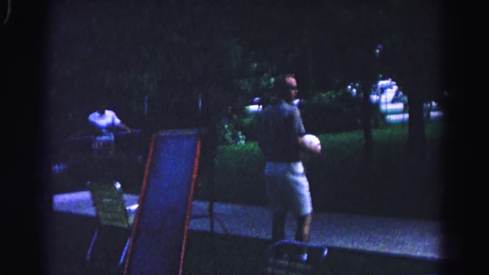 Man in shorts holding white ball near a children's slide in a nighttime backyard, Hagerstown, Maryland, circa 1963; second figure and folding chair visible behind him.