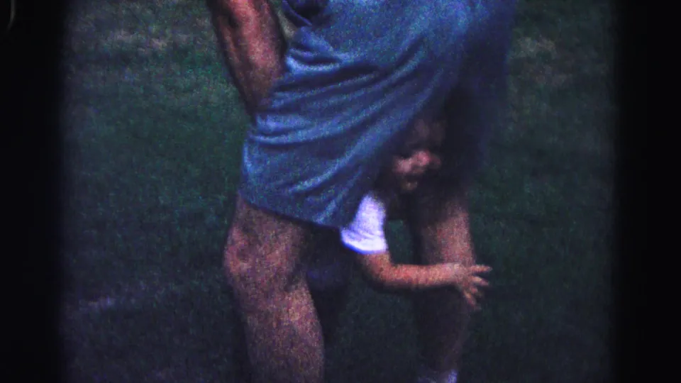 Close-up of a young child in white top clinging to an adult's legs in a nighttime backyard, Hagerstown, Maryland, circa 1963.