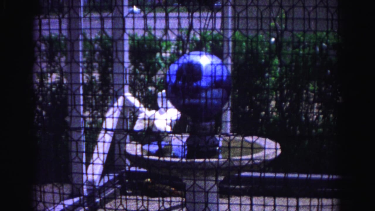 Blue ornamental globe fountain on white pedestal basin viewed through wire mesh enclosure, 8mm home movie, Hagerstown Maryland, 1963