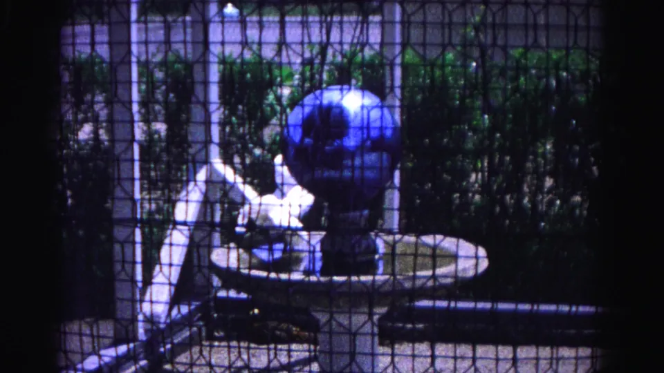 Blue decorative globe fountain on white pedestal through wire mesh enclosure, 8mm home movie, Hagerstown Maryland, 1963