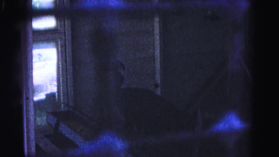 8mm home movie frame circa 1963, severely underexposed, with interior steps, a light source at the left edge, and prominent blue prismatic film artifacts; Hagerstown, Maryland.