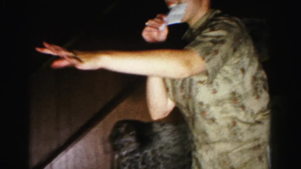 Extreme close-up of a woman's reaching arm beside the floral armchair during a cushion-placement action; 1963 8mm home movie, Hagerstown, Maryland.