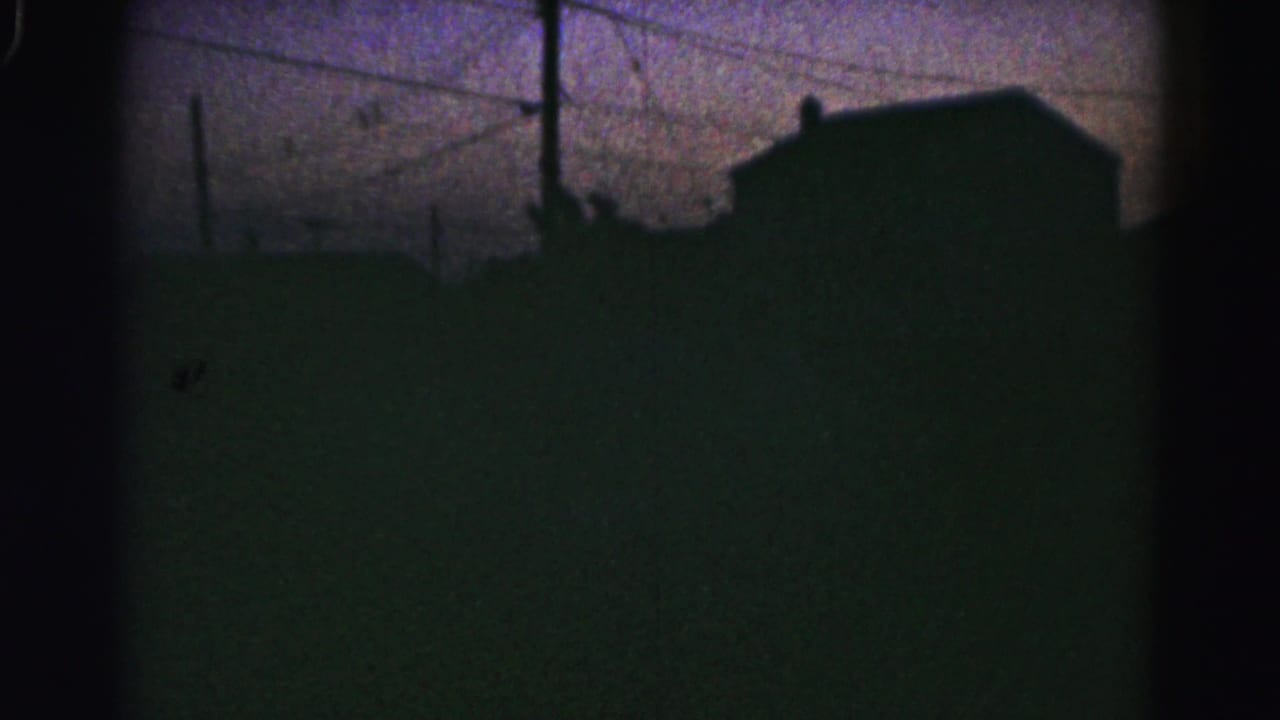 Silhouetted rooftops and power lines beneath a dim twilight sky.