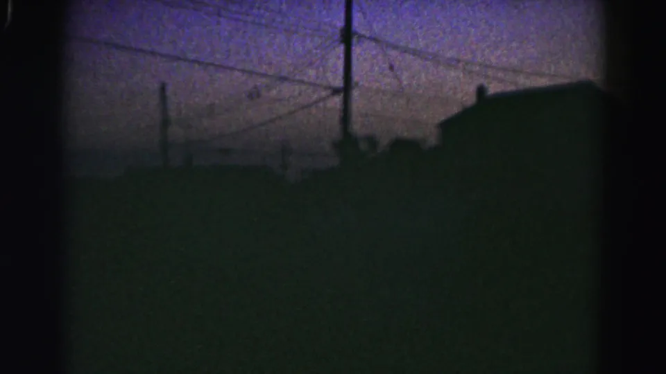 Grainy 1963 Hagerstown frame with utility poles, wires and low house silhouettes in twilight.