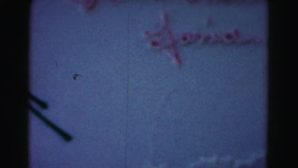 1963 Hagerstown home-movie frame showing a white frosted birthday cake with red icing writing and a small yellow decoration in soft focus.