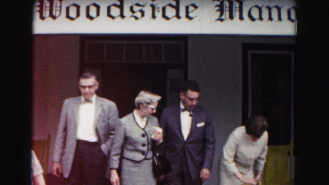 Formally dressed adults exit a porch beneath a partial Woodside Man sign.