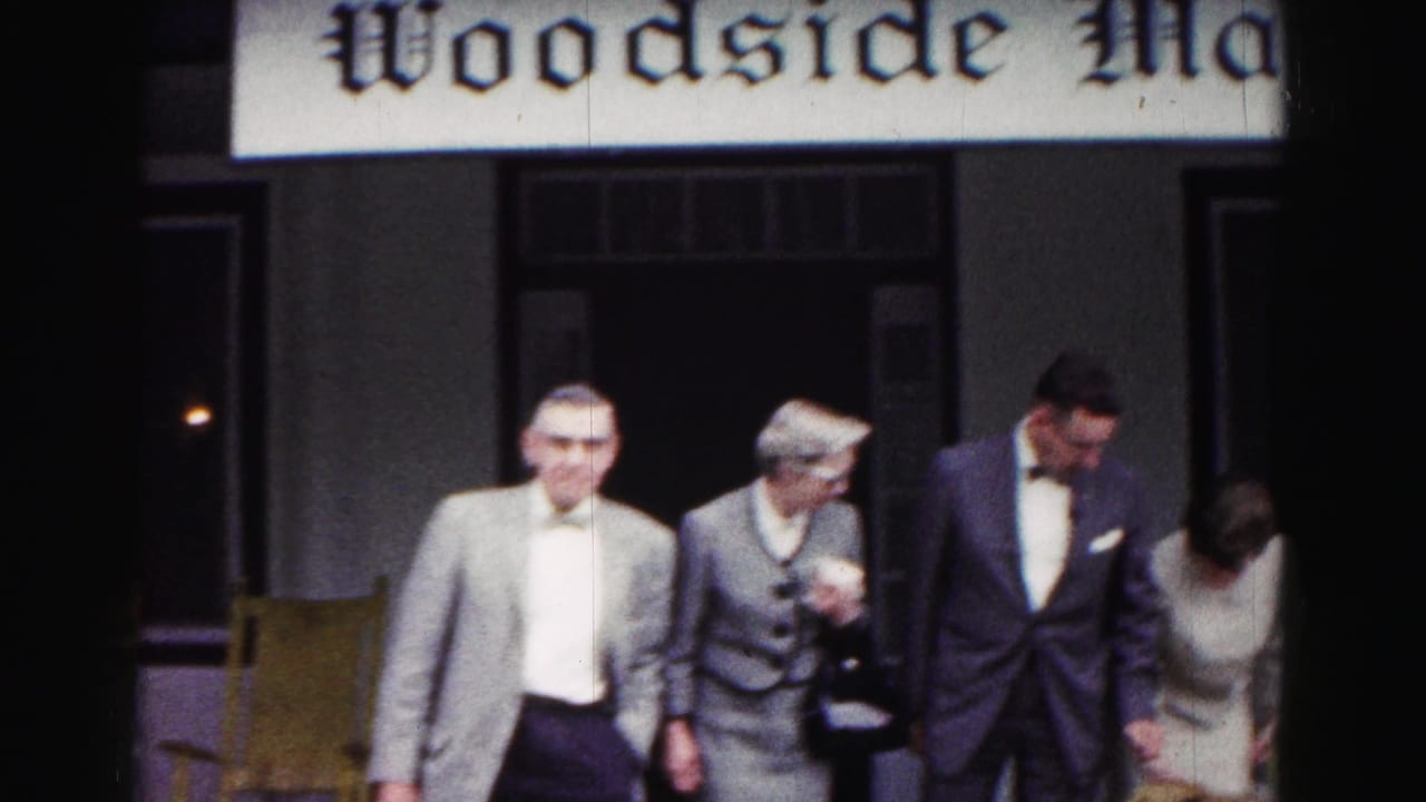 A group of adults in suits and dress clothing moves across a porch in the 1963 Hagerstown home-movie footage.
