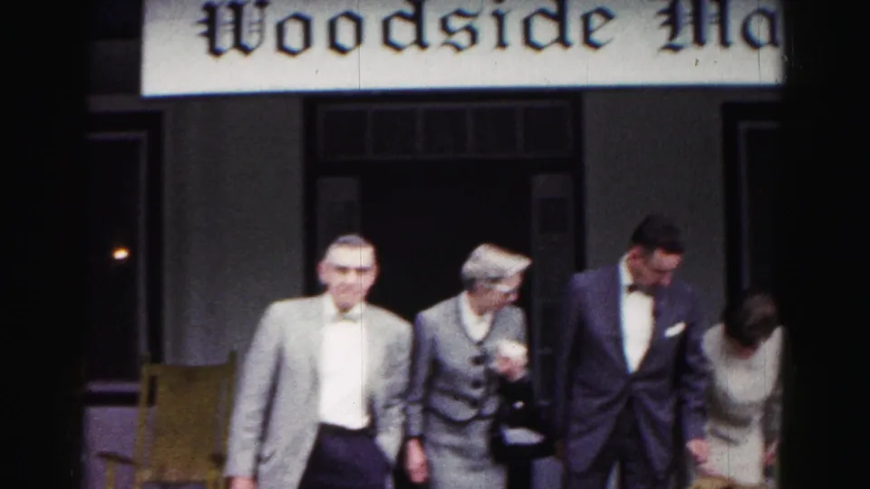 A group of adults in suits and dress clothing moves across a porch in the 1963 Hagerstown home-movie footage.