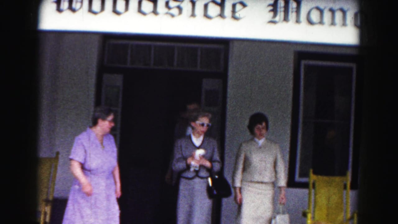 Women in formal clothing standing outside a doorway below a Woodside Manor sign.